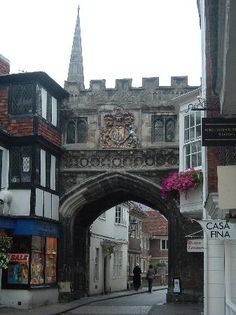 an arch in the middle of a street with buildings on both sides and people walking under it