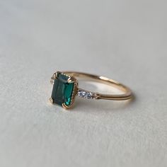 an emerald colored ring with two diamonds on it's sides, sitting on a white surface