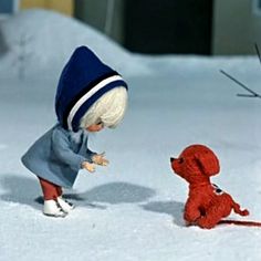 a small doll is playing with a red dog in the snow while another toy looks on