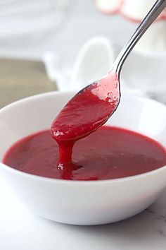 a spoon full of red sauce in a white bowl