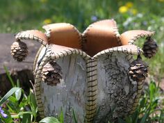 a basket made out of wood with pine cones on it sitting in the grass next to some flowers