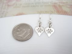 "Paw Print Earrings Simple sterling silver Paw Print Heart Earrings features a little paw print cut out of a sterling silver heart charm. Dainty and super cute! EARRING DETAILS ~ Your Choice of .925 Sterling Silver Standard Hook, Kidney, or Lever Back Ear Wire ~ Sterling Silver Paw Print Heart Charm Measurements (inches): Length: 0.51 Width: 0.31 Measurements (mm): Length: 13 Width: 8 Earrings hang approximately 1 inch from the top of the ear wire to the bottom of the heart on standard french ho Personalized Heart-shaped Sterling Silver Earrings, Personalized Sterling Silver Heart Earrings As Gift, Personalized Sterling Silver Heart Earrings For Valentine's Day, Mother's Day Nickel Free Sterling Silver Heart Earrings, Pet Earrings, Tiny Paw Print, Paw Print Heart, Paw Print Earrings, Printed Jewelry