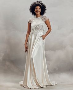 a woman in a long white dress posing for a photo with clouds behind her,