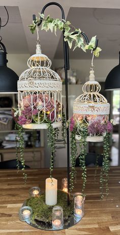 two birdcages with flowers and greenery hanging from them on top of a table