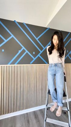 a woman standing on top of a ladder in front of a wall with blue lines