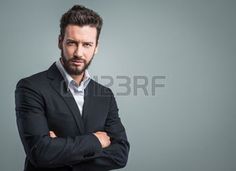 a man in a suit with his arms crossed looking at the camera while standing against a gray background