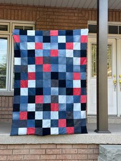 a blue, red and black quilt sitting on top of a brick wall next to a white door