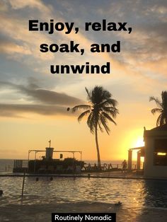 the sun is setting behind some palm trees and people are swimming in the pool at sunset