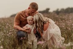 a man, woman and baby are sitting in the middle of a field with wildflowers