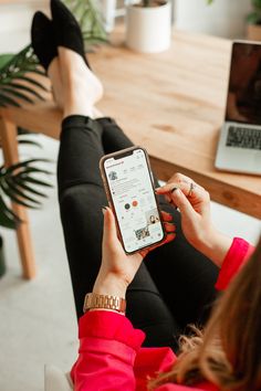 a woman is sitting on the couch and looking at her cell phone while she sits in front of a laptop