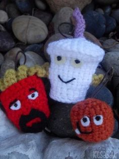 three crocheted items sitting on top of rocks next to each other, with faces drawn on them