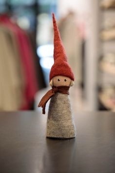 a small doll sitting on top of a table next to a piece of cloth with a red hat