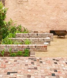 an empty bench sitting next to a brick wall and planter in front of it