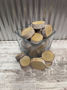 a glass bowl filled with wood slices on top of a wooden table next to a metal wall