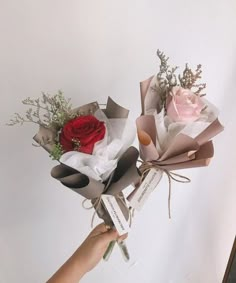 someone is holding two roses in their hand and the flowers are wrapped in brown paper