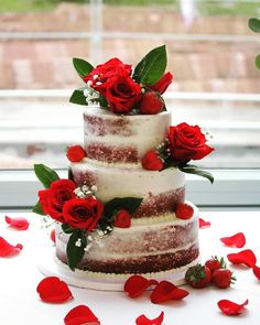 a three tiered cake with red flowers and greenery on the top is surrounded by petals