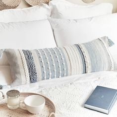 a white bed topped with pillows next to two cups and a tray filled with food