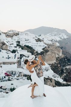 a man and woman standing on top of a roof next to each other in front of white buildings