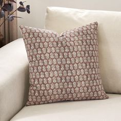 a brown and white pillow sitting on top of a couch next to a vase with flowers