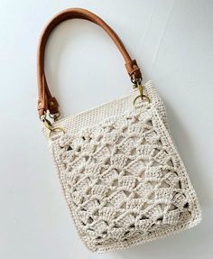 a white crocheted bag hanging on the wall with a brown leather strap around it