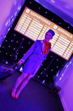 a woman standing in front of a projection screen holding a luggage bag and smiling at the camera