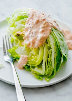 a white plate topped with lettuce covered in ranch dressing next to a fork