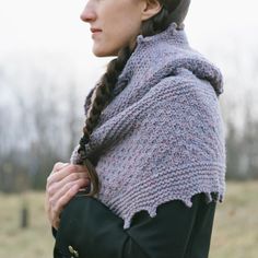 a woman with braids wearing a knitted shawl in a field, looking off to the side