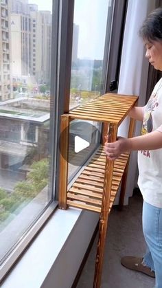 a woman standing next to a window with a wooden shelf on it's side