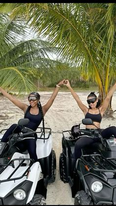 two women on four wheelers with palm trees in the backgroung and one holding her arms up