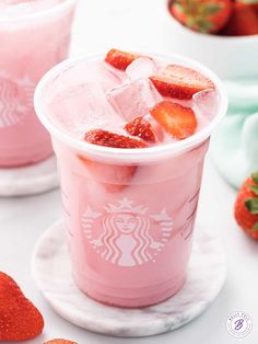 two cups filled with ice and strawberries on top of a white table next to bowls of strawberries