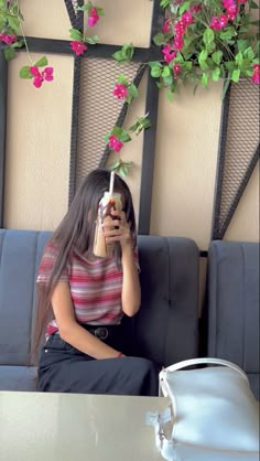 a woman sitting on a couch holding a cell phone up to her face with pink flowers in the background