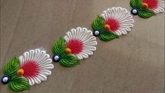 three colorful flowers on a table with white and green leaves in the center, along with blue beads