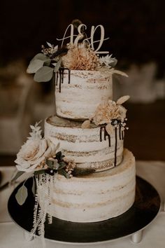 a wedding cake with white frosting and flowers on top sits on a black plate