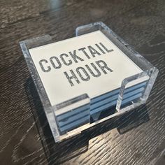 a wooden table topped with a plastic container filled with drinks and writing on it that says cocktail hour