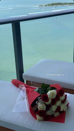 a bouquet of roses sits on the edge of a bed with an ocean in the background