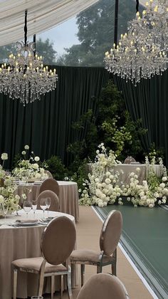 an elegant wedding setup with chandeliers and white flowers on the table, surrounded by greenery