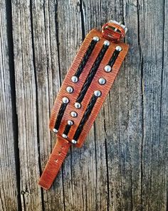 a leather belt with metal rivets on it sitting on a wooden planked surface