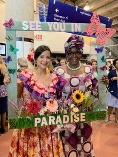 two women standing next to each other in front of a sign that says paradise and butterflies