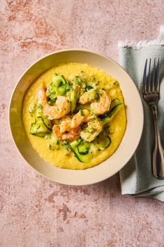 a white bowl filled with shrimp and zucchini grits next to a fork