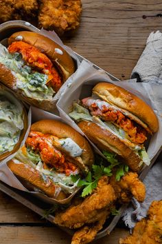 four chicken sandwiches in takeout containers with cole slaw and sauce on the side