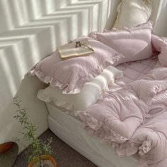 an unmade bed with pink comforter and pillows on it next to a potted plant