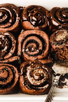 chocolate cinnamon rolls with icing and powdered sugar in a white dish next to a spoon