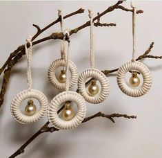 four ornaments hanging from a tree branch with white rope and gold pearls on it's ends