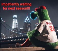 a green mascot sitting on top of a wooden fence next to a cityscape