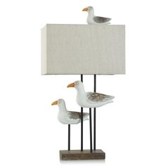 two seagulls are standing next to a lamp on a white surface with a linen shade