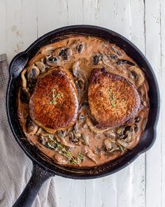 two pork chops covered in mushroom gravy in a cast iron skillet