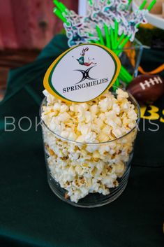 a bowl filled with popcorn sitting on top of a green table cloth next to a football