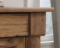 a close up view of a wooden dresser with the drawer open and curtains in the background