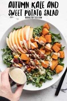 a white plate topped with sliced apples and salad next to a hand holding a cup