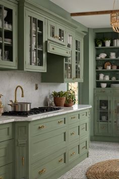 a kitchen with green cabinets and white marble counter tops, gold pulls on the handles